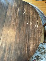 Close-up of table surface showing scratches and marks indicating wear, dark wood grain finish.