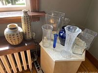 10 assorted vases on surfaces near window: 2 pottery vases with Chinese script, 1 cut crystal vase, 7 various glass vases including clear and blue glass