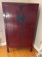 Front view of the red distressed cabinet featuring large circular black metal clasp and metal handles on doors.
