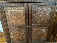 Close up of the carved door details on the cabinet showing intricate heraldic and floral carvings.