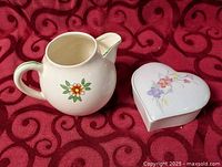 Pitcher and heart box side by side on red patterned cloth