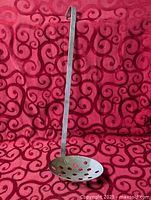 Full view of metal ladle showing handle and perforated scoop