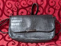 Front view of crocodile-embossed leather clutch showing flap and silver-tone bar
