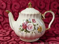 Full left side view of floral porcelain teapot showing lid, handle, spout and gold trim