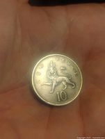 Front side of the coin showing a lion with 'TEN PENCE' and '10' inscriptions, held in hand against a dark background.