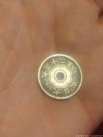 Front side of Asian silver coin showing floral petal pattern, central hole, and Asian characters.