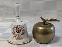 Photo showing both items side by side: the porcelain bell with Charles and Diana image and the brass apple.
