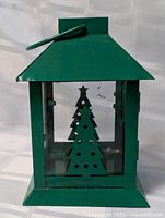 Front view of green metal candle lantern with Christmas tree design on glass panels