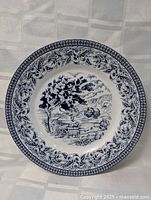 Full view of the porcelain plate showing the detailed blue scenic transferware design with a tree, wagon, ship, and landscape, with a patterned floral border.