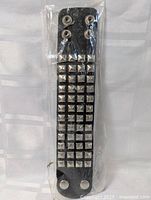 Photo of black leather wristband bracelet with multiple rows of silver-tone metal pyramid studs still in plastic packaging.