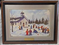 Framed print showing winter outdoor scene with old stone schoolhouse and children playing in snow. Wood frame with brass plaque attached.