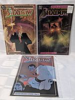 Three comic books from The Shadow series, individually sleeved, standing and lying on a white surface in bright natural light.