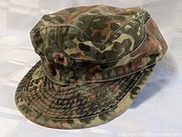 View of military camouflage cap showing fabric pattern, visor, and ventilation eyelets.