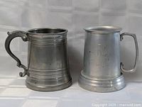 Two pewter tankards side by side on neutral background, showing general size and style differences.