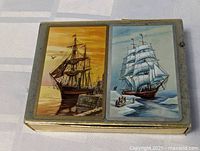 Top view of two decks of playing cards and tin box, showing tall ship artwork on cards.