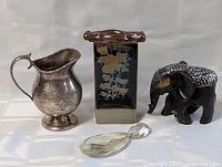 Front view of the lot showing the pottery vase, pewter pitcher, wooden elephant figurine, and crystal ornament.
