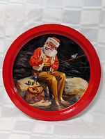 Full view of the round tin tray depicting Santa Claus fishing, showing bright red rim and detailed colored illustration.