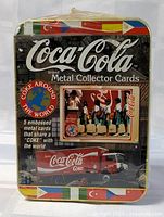 Front view of sealed Coca-Cola metal collector cards tin with logos, images and flags visible