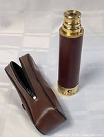 Brass and brown leather-covered telescopic telescope standing upright with the carrying pouch beside it.