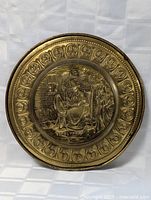 Top view of the round brass wall plate showing detailed embossed scene with woman and ornate border.