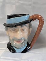 Front view of the Toby Jug mug showing the man's face with a black hat with a blue band, painted gray beard and mustache, and brown handle.