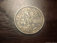 Reverse side of the 1961 UK six pence coin showing floral design with inscriptions and denomination.