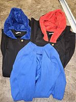 All three coats laid flat: black with blue faux-fur hood, black with red faux-fur hood, blue collarless coat