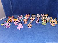 Front view of all 17 Littlest Pet Shop figures lined up on blue background