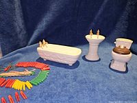 Bathtub, pedestal sink, toilet, coloured clothespins and line laid out on blue surface