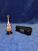 Miniature guitar on metal stand next to closed black case