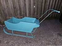 Side view of blue wooden sleigh showing metal push handle and runners