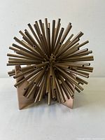Front view of abstract starburst sculpture showing metal rods protruding from center and metal angled base.