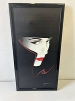 Framed signed art print on canvas showing a stylized close-up of a woman's face with a black hat and coat with red highlights.