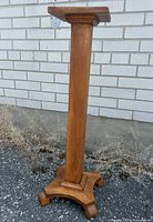 Full view of the antique oak plant stand showing the straight column and square top against a brick wall.