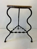 Front angle showing the wrought iron legs with a twisted stretcher and round wooden seat