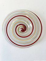 Top-view photo of round Murano glass bowl with colorful concentric spiral bands in red, yellow, blue, white and other colors, glossy finish