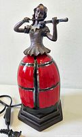 Front view of the lamp showing the lady playing violin and the red glass shade skirt on hexagonal base.