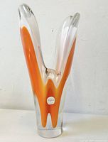 Front view of the orange and clear tooth-shaped glass vase with original Flygfors label on base.