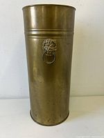 Full front view of the brass umbrella stand showing cylindrical shape and lion head handle.