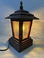 Pagoda form wooden table lamp illuminated, showing textured glass panels, base, and electrical cord.