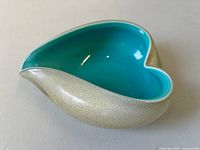 Heart-shaped Murano glass bowl showing turquoise interior and textured off-white exterior, curved form