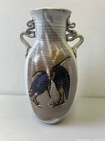 Front view of the tall, hand-thrown pottery vase showing two dark blue birds painted on, with sculpted double handles on each side and earthy toned glaze with textured horizontal lines.