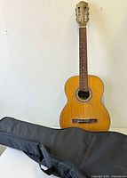 Full front view of vintage Carmencita wooden acoustic guitar standing behind the black back pack case.