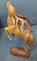 Side view of the wooden leaping stag deer sculpture showing detailed carving and natural wood finish.