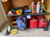 Two shelves filled with assorted auto supplies including cans of polish, wax, two red plastic fuel containers, a funnel, and small ramps