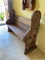 View of entire oak wood church pew with carved Gothic style end panel and armrest detailing, showing the full length and seating area.