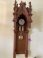 Front view of the antique Gothic wall clock with visible clock face, pendulum, and weights inside ornate wooden case.