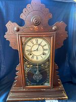 Front view of antique Waterbury Clock Co. mantle clock showing wooden case with carved top and sides, glass door with decorative gold design, and Roman numeral clock face.