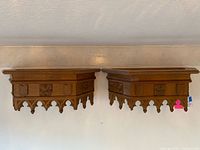 Pair of antique wood carved wall shelves with Gothic pointed arch carvings and shield panels from Germany shown mounted side by side on wall.