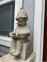 Full side view showing entire statue of child sitting on block holding bird feeder dish with bird.